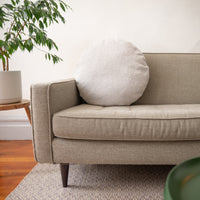 Beige sofa with a round white pillow in a living room setting