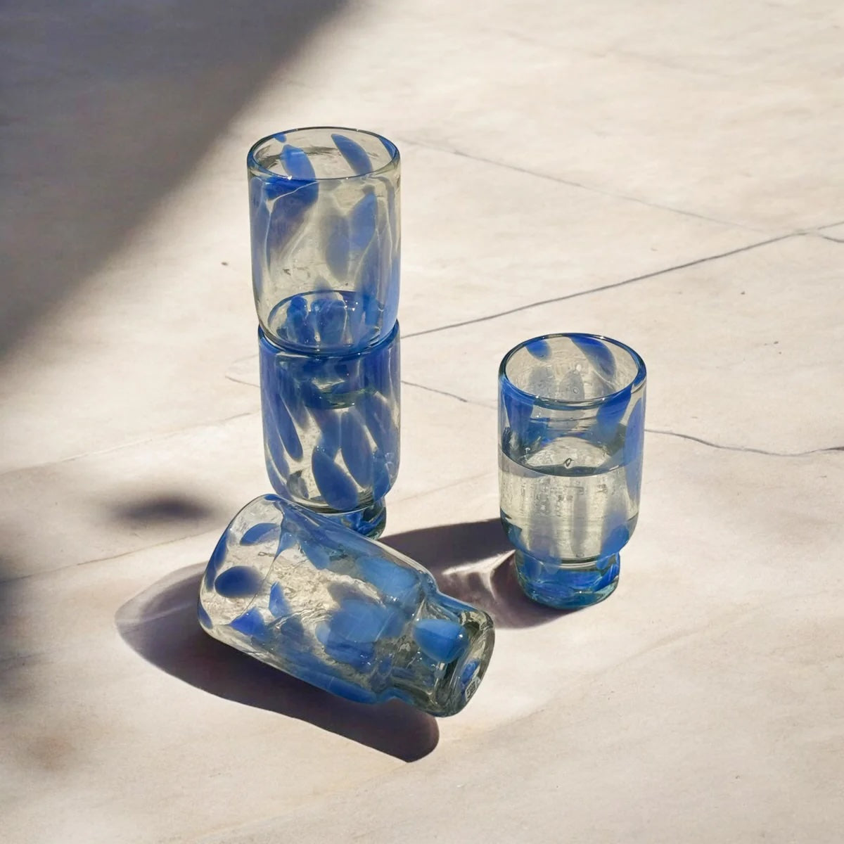 Four blue drinking glasses on a light-colored surface with shadows.
