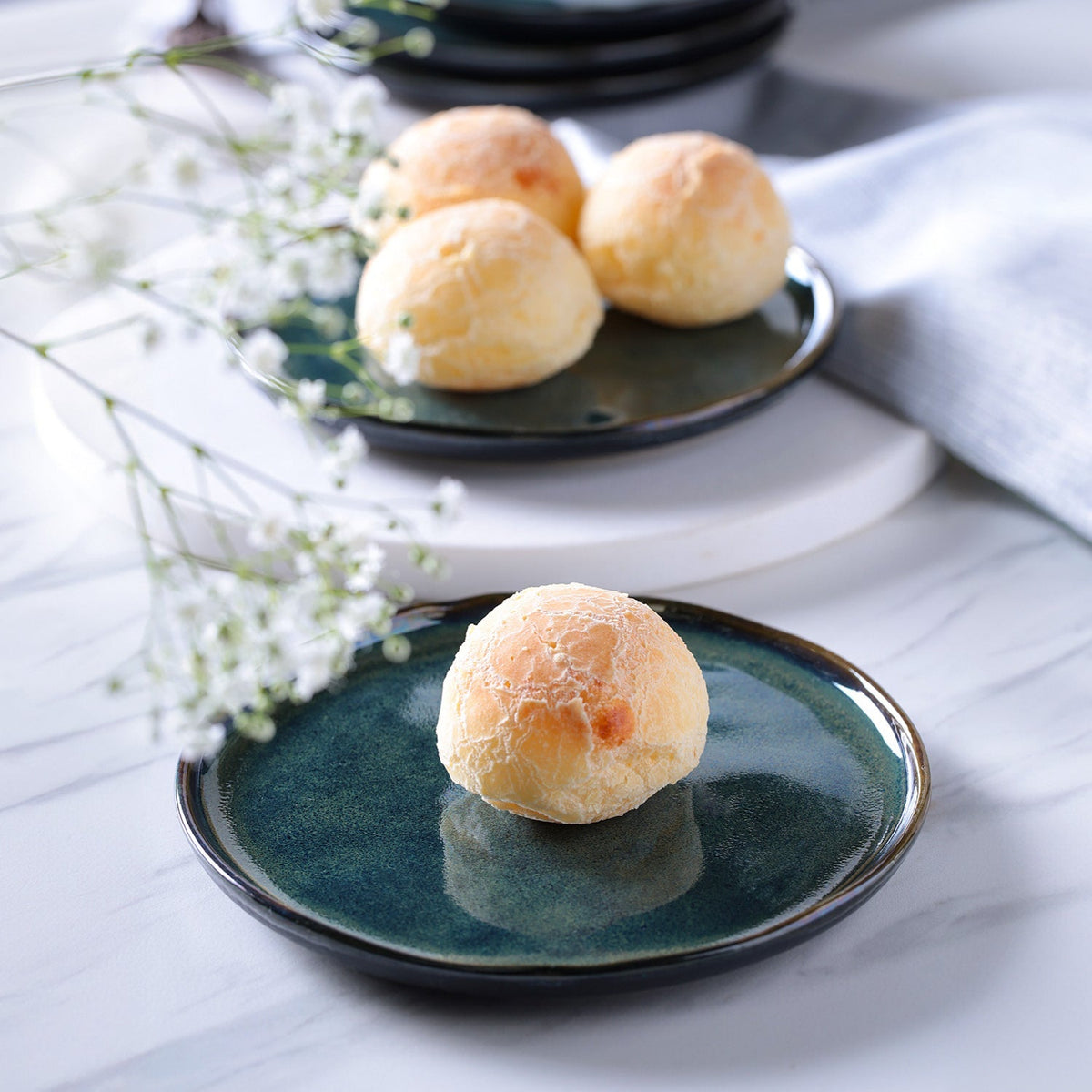 Three round pastries on a green ceramic plate with white flowers in the background.