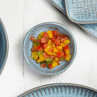 Colorful chopped peppers in a blue ramekin on a white surface with additional blue dishes.