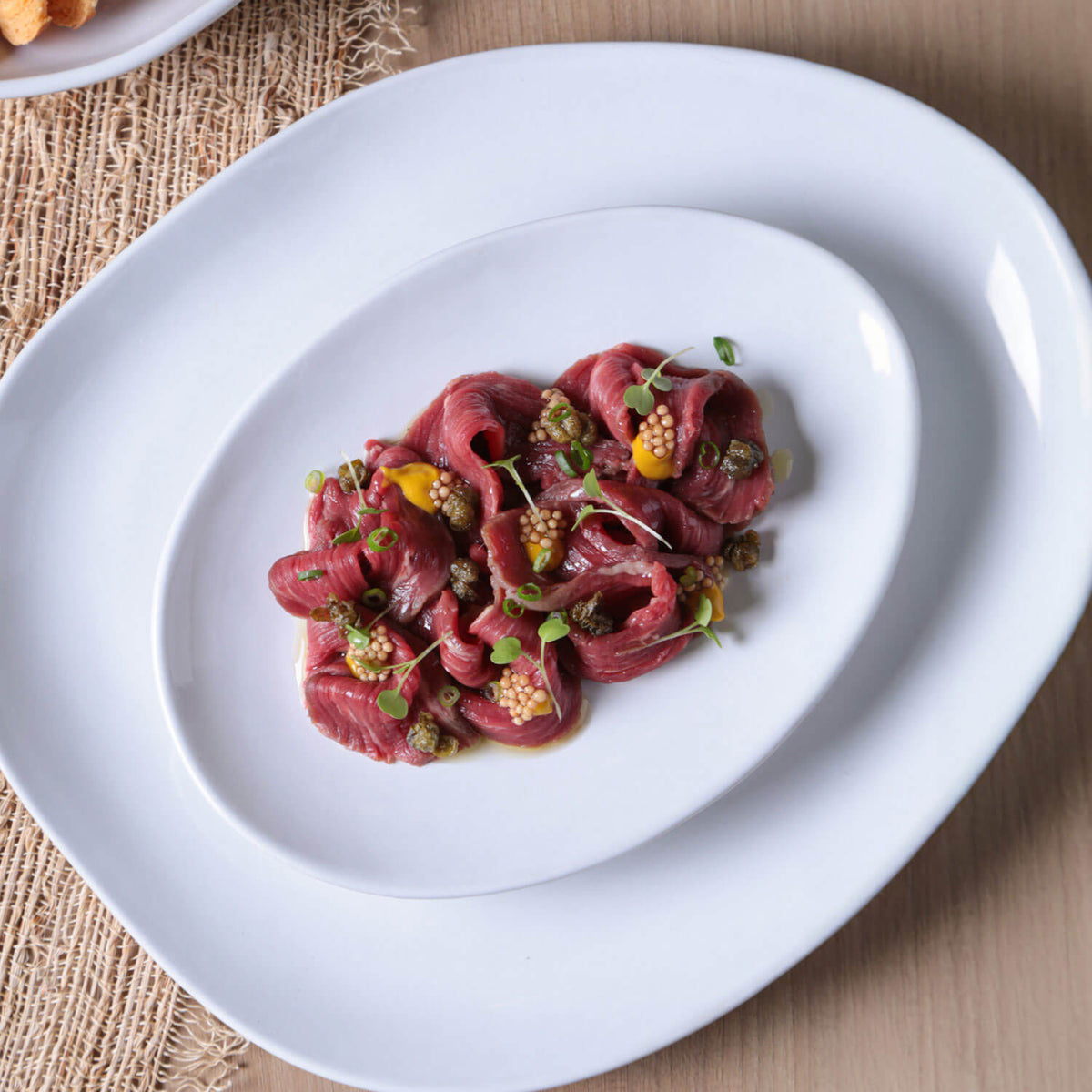 Plated dish of red meat with garnishes on a white plate