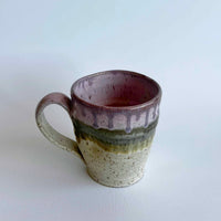 Ceramic mug with light and dark neutral and pink glaze details on a white background