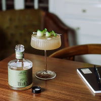 Cocktail in a glass with a bottle labeled 'Tilden' on a wooden table.