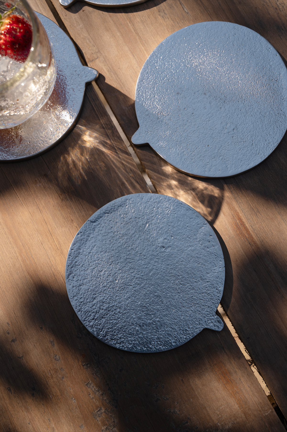 Silver round coasters on a wooden surface with a glass of water and a strawberry.