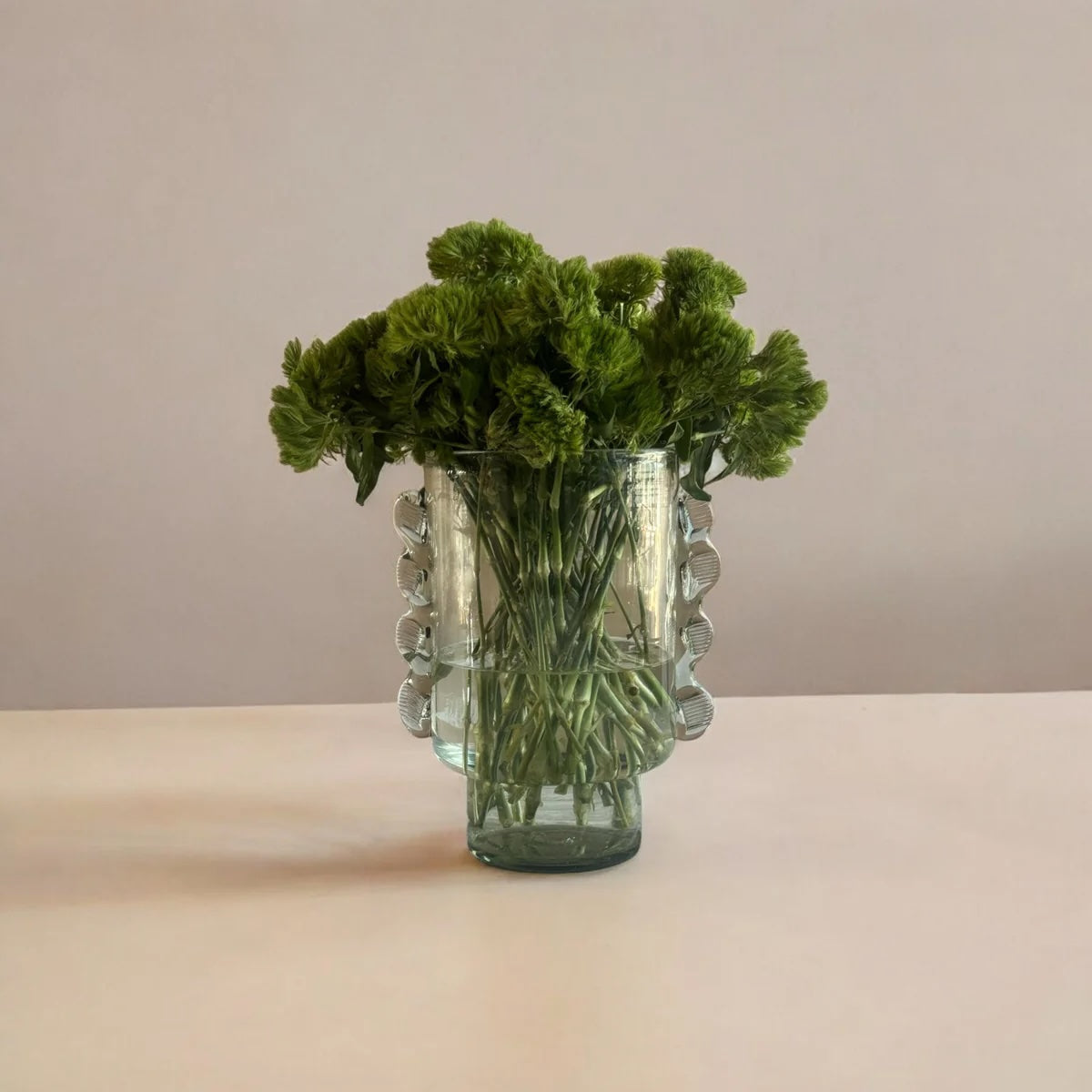 Glass vase with green foliage on a beige surface and background