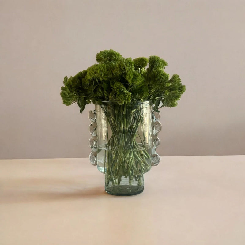 Glass vase with green foliage on a beige surface and background