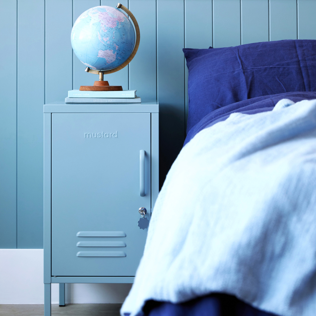 Blue locker style nightstand with a globe on top next to a bed with blue bedding.