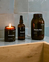 A lit candle, spray bottle, and glass jar set on a tiled surface with black labels