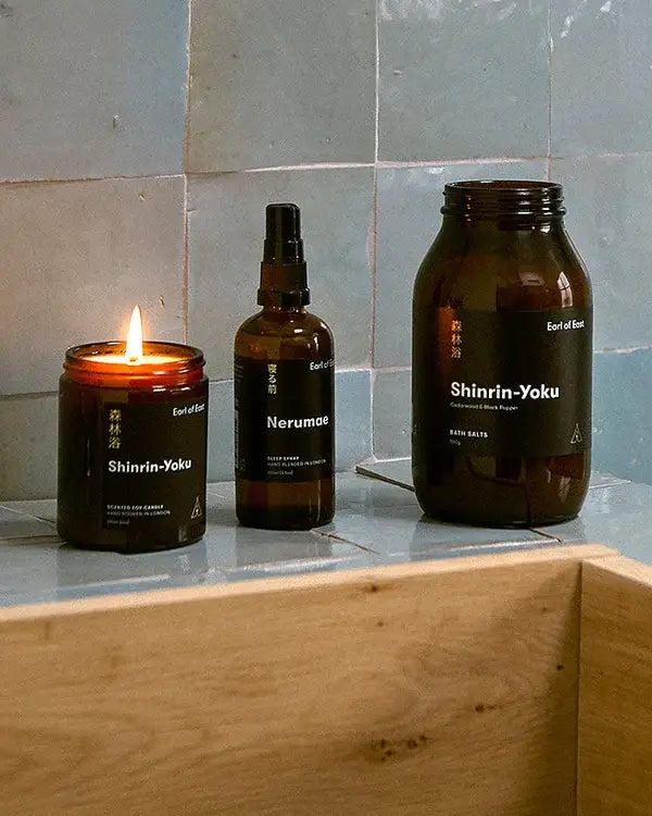 A lit candle, spray bottle, and glass jar set on a tiled surface with black labels