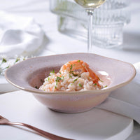 Pink ceramic bowl of risotto with shrimp on a white tablecloth