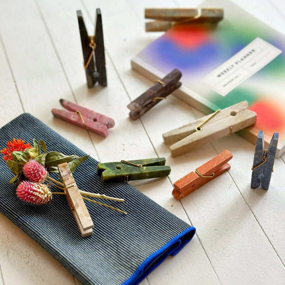Colorful stone clothespins on a white surface with a blurred book and cloth napkin in the background.