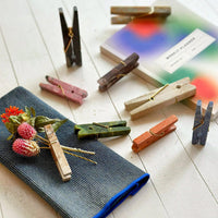 Colorful stone clothespins on a white surface with a blurred book and cloth napkin in the background.