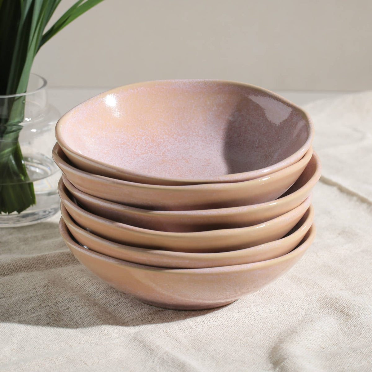 Stack of pink ceramic bowls on a light surface with a vase in the background