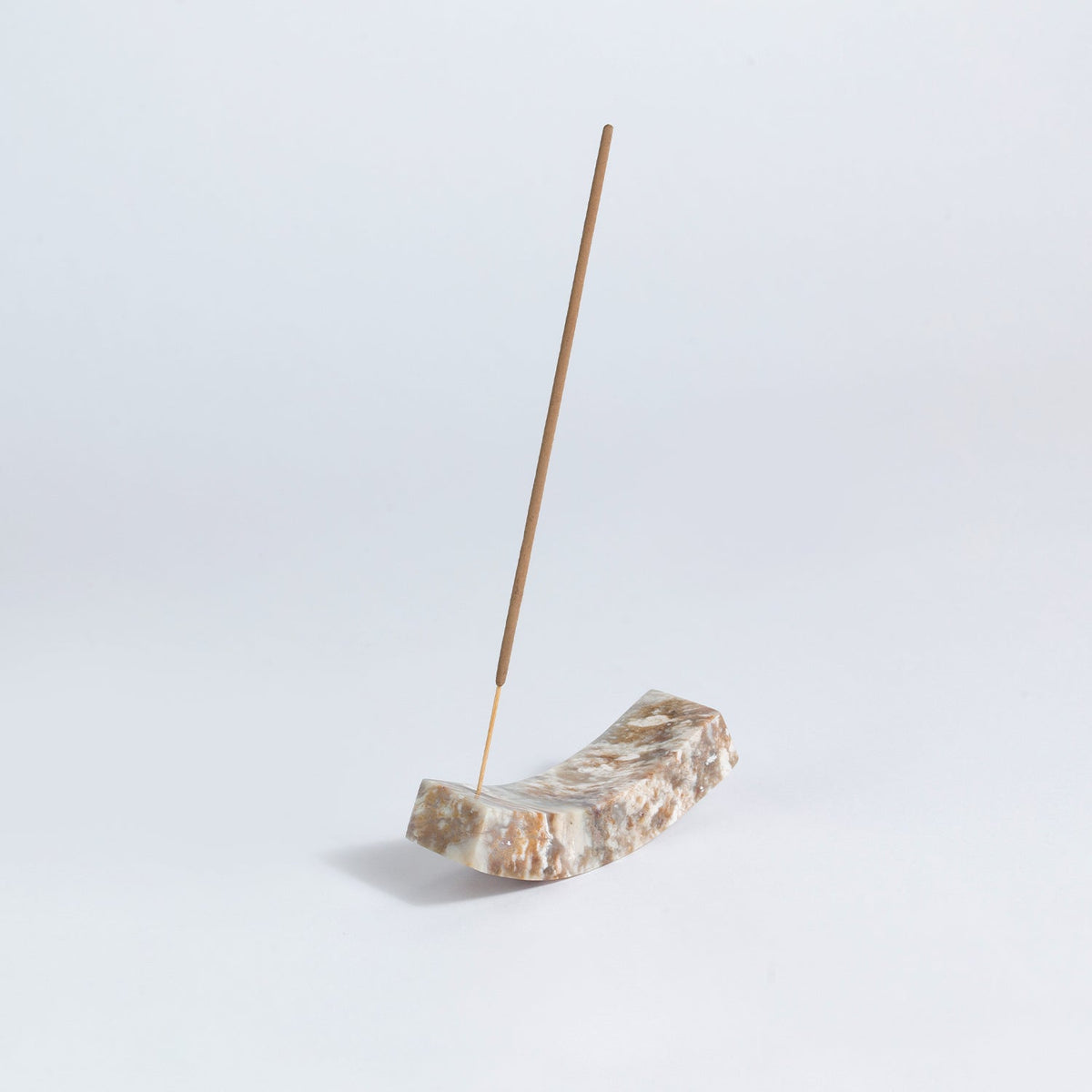 Incense stick on a curved natural stone holder against a light gray background