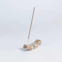 Incense stick on a curved natural stone holder against a light gray background