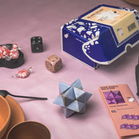 Stone star puzzle, dice, and packaging on a pink surface