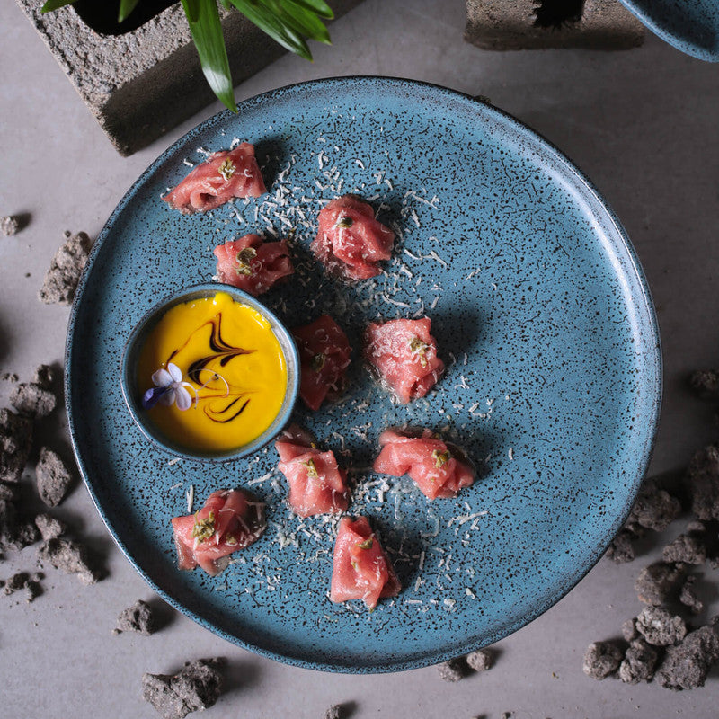 Blue plate with raw meat bites and a yellow sauce on a textured surface
