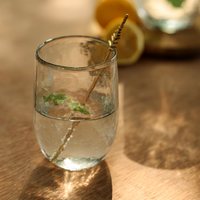 Pebbled drinking glass with a stir stick on a wood surface