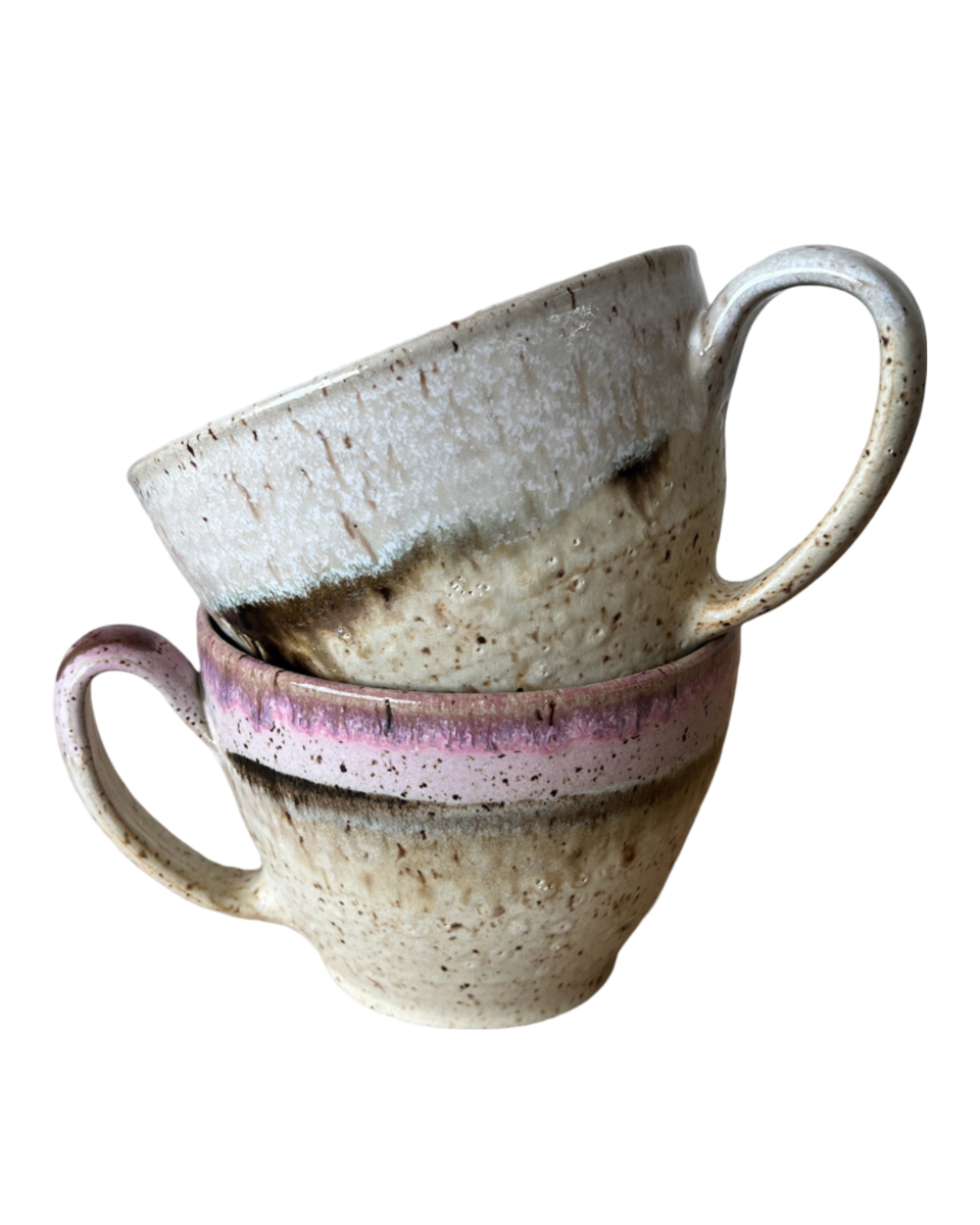 Two stacked ceramic mugs with light and dark neutral and pink glaze details on a white background