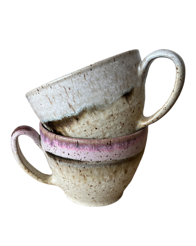 Two stacked ceramic mugs with light and dark neutral and pink glaze details on a white background