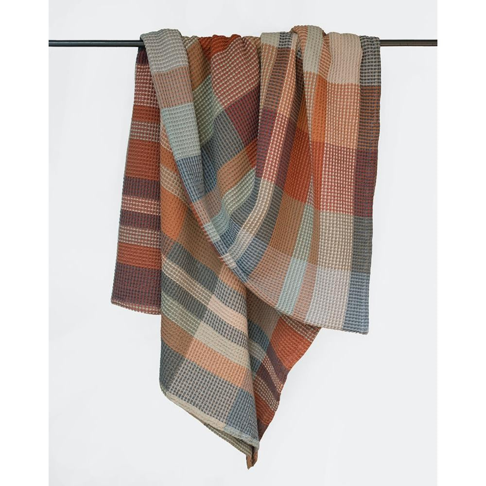 Plaid waffle weave blanket with autumnal colors draped over a rod 