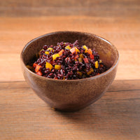 Brown bowl with black rice and vegetables on a wooden surface