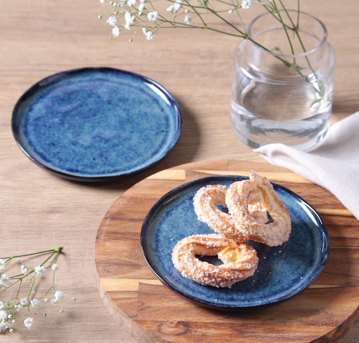 Blue ceramic plate with pastries on a wooden board, accompanied by a blue ceramic dish and a glass of water.