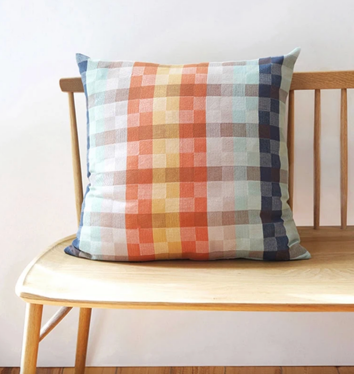 Plaid pillow on a wooden bench against a white wall