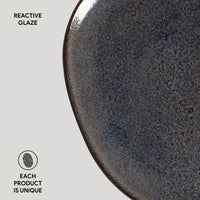 Close-up of a dark ceramic plate with reactive glaze on a light gray background