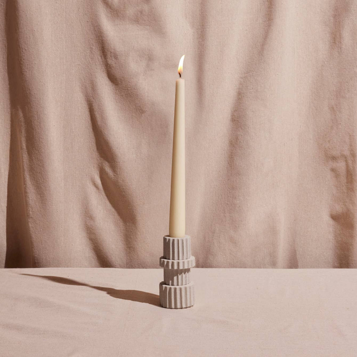 Candle in a textured holder against a beige curtain