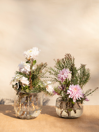 Two glass vases with floral arrangements on a beige surface and background
