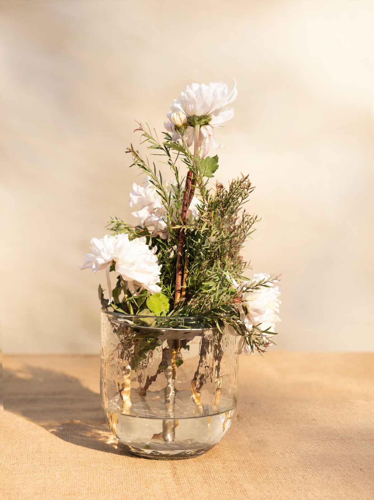 Clear glass vase with white flowers and greenery on a wooden surface with a neutral background
