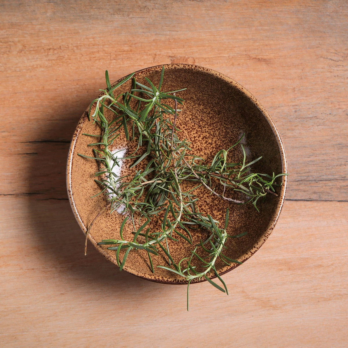 Herbs in a brown ceramic bowl on a wooden surface