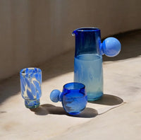 Set of blue glassware including a pitcher and two tumblers on a cement surface.
