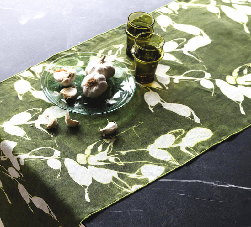 Green floral table runner with garlic bulbs and olive oil glasses on a marble surface