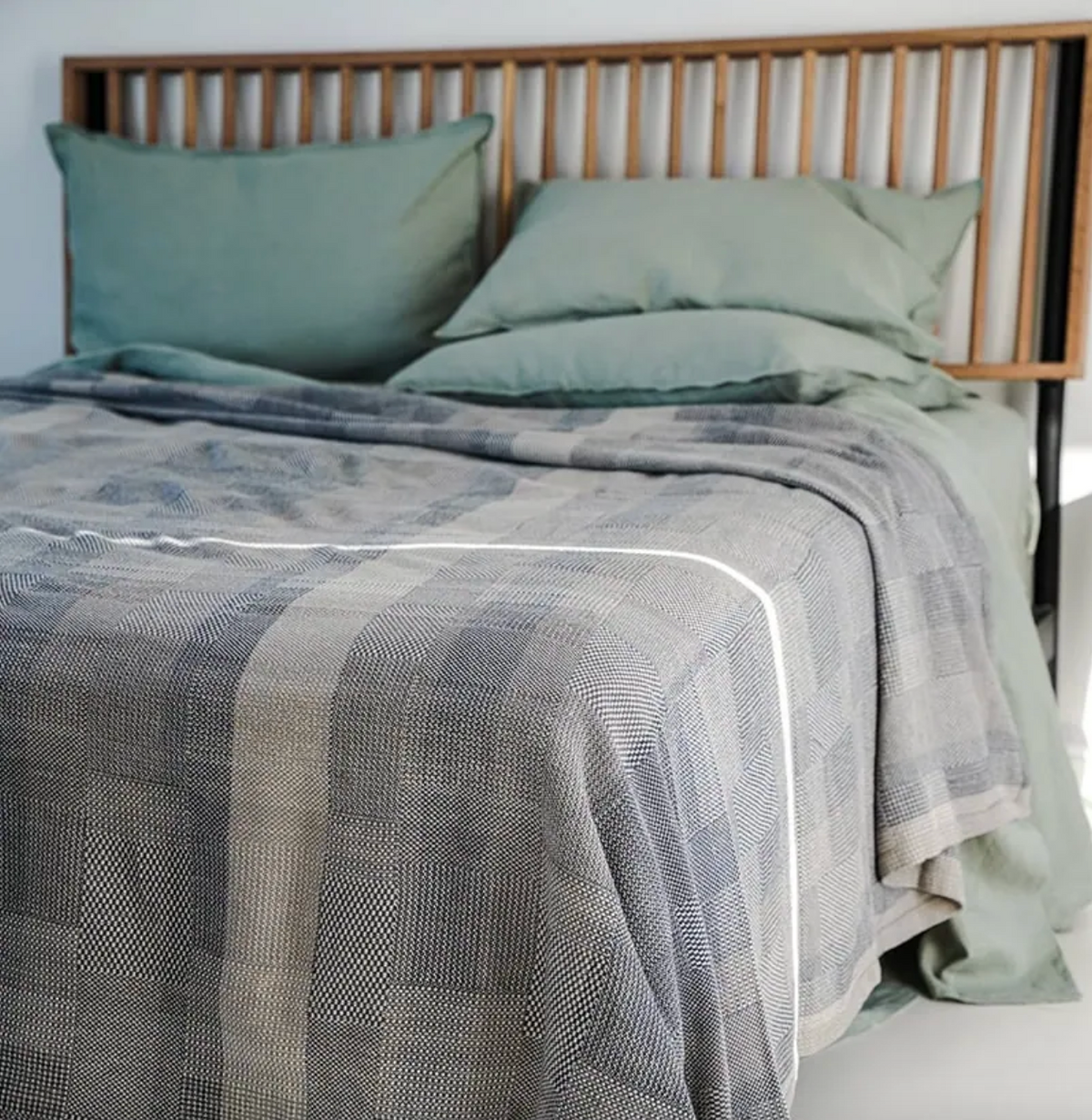 Bed with green sheets and a textured gray blanket in a bedroom setting.