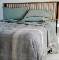 Bed with green sheets and a textured gray blanket in a bedroom setting.