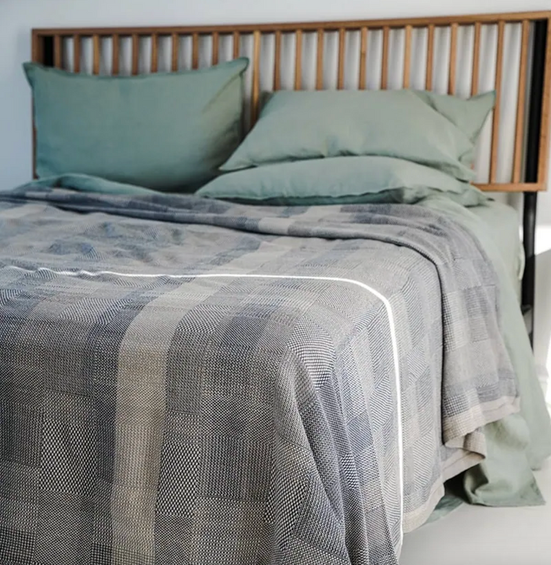 Bed with green sheets and a textured gray blanket in a bedroom setting.