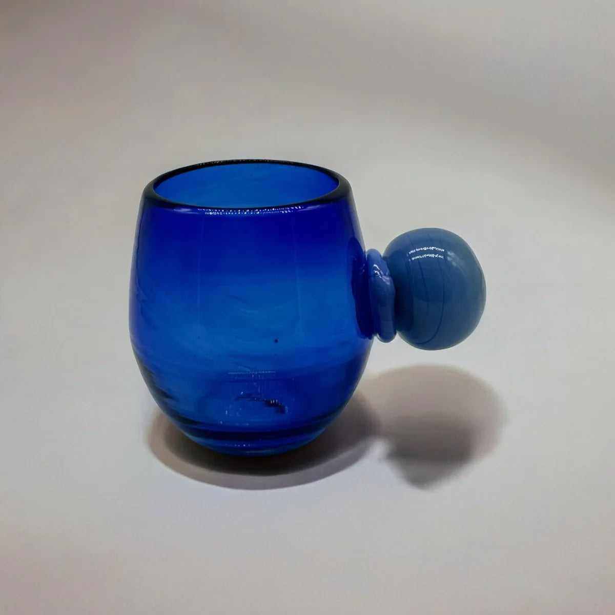 Blue glass tumbler with a spherical handle on a light background
