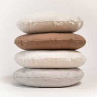 Stack of four round cushions in beige, brown, and gray on a light background