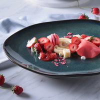 Blue plate with dessert featuring strawberries and macarons on a marble surface.