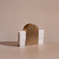 Gold arch-shaped napkin holder on a beige surface with a plain background