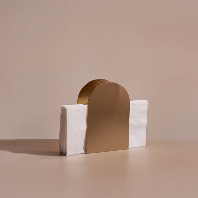 Gold arch-shaped napkin holder on a beige surface with a plain background