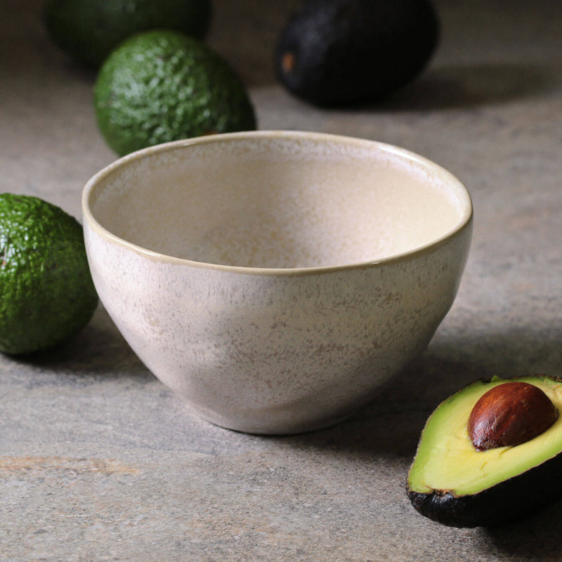 Beige ceramic bowl on a stone surface with whole and sliced avocados.