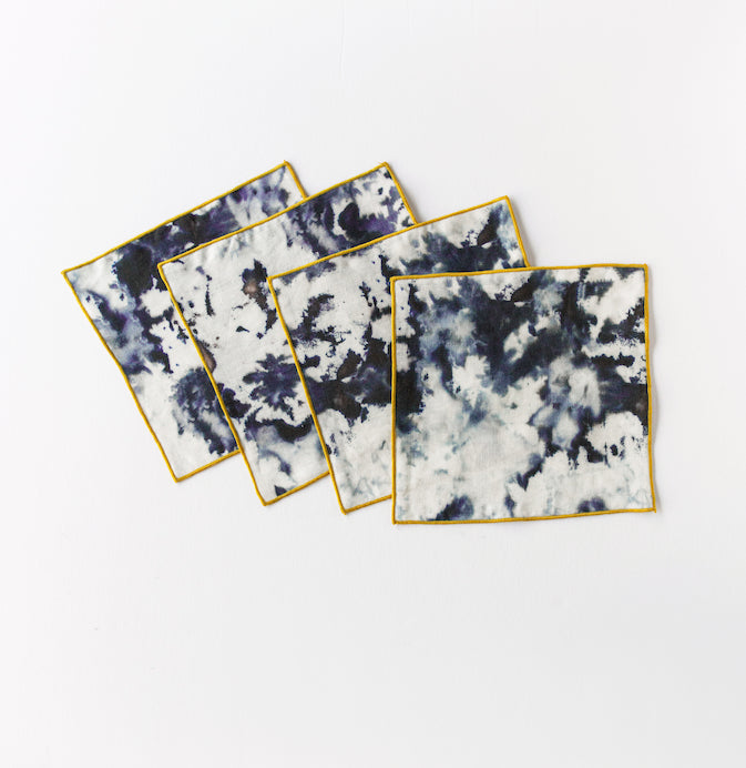 Set of four tie-dye cocktail napkins with gold edges on a white background