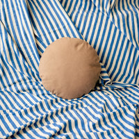 Round light brown pillow on a blue and white striped fabric background