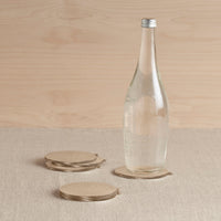 Clear glass bottle with metal cap on a beige surface with brass coasters and a wooden background