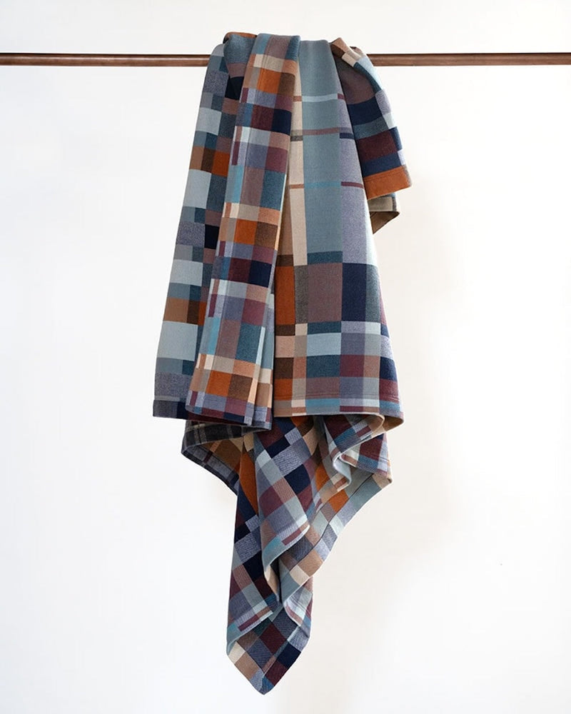 Plaid multi-color blanket draped over a wooden rod