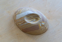 A small oval nerikomi porcelain dish with concentric wavy bands of tan, brown, cream, and pale yellow, photographed on a light wood surface.