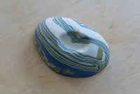 A small oval nerikomi porcelain dish with concentric wavy bands of blue, green, and white, photographed on a light wood surface.